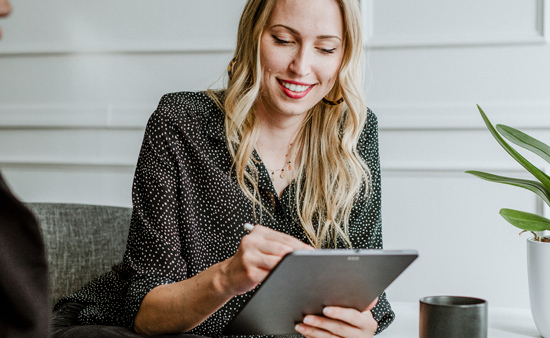 smiling woman using tablet while sitting on couch with plant and coffee cup 15 ways to engage