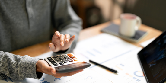person using a calculator while reviewing business documents and financial graphs with a coffee cup present in the workspace focused on calculations and effective financial planning 3 finance methods