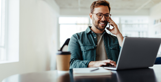 smiling man talking on phone while working on laptop at a desk with coffee cup showing effective multitasking and productivity 2 active engagement