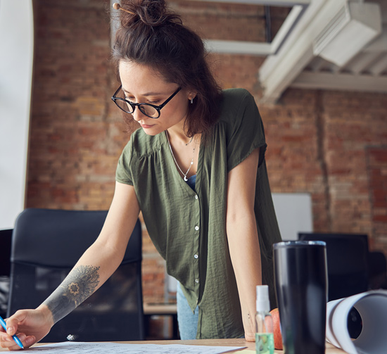 young woman writing on paper in a modern office focused on her work with a green shirt and glasses office productivity design