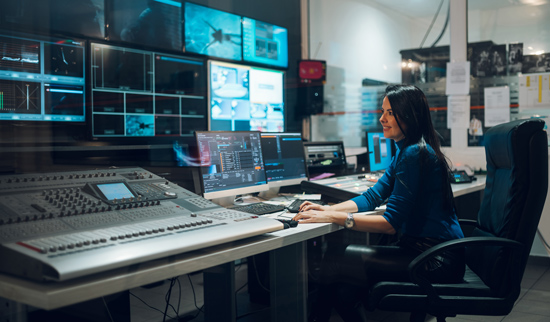 woman operating broadcast equipment in a control room managing video production three screens connected