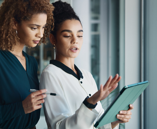 two women discussing work while looking at a tablet in a modern office setting collaboration brainstorming ideas