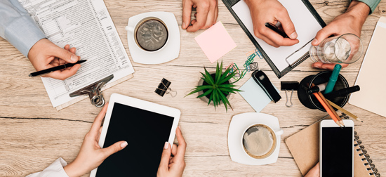 hands working on documents and tablets with coffee and plants in a business meeting setting two professionals collaborating