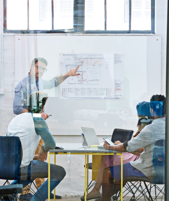 man pointing to a map during a meeting with three people at a table in a modern office setting